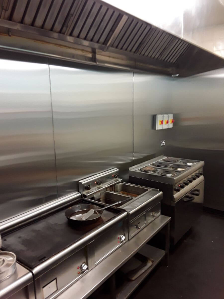 Inside a busy cafe kitchen, stainless steel walls and canopy